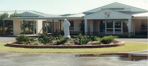 School building with a garden and a central statue in front